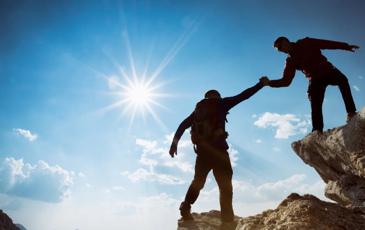 Two people supporting each other on a mountain - teamwork and shared achievement